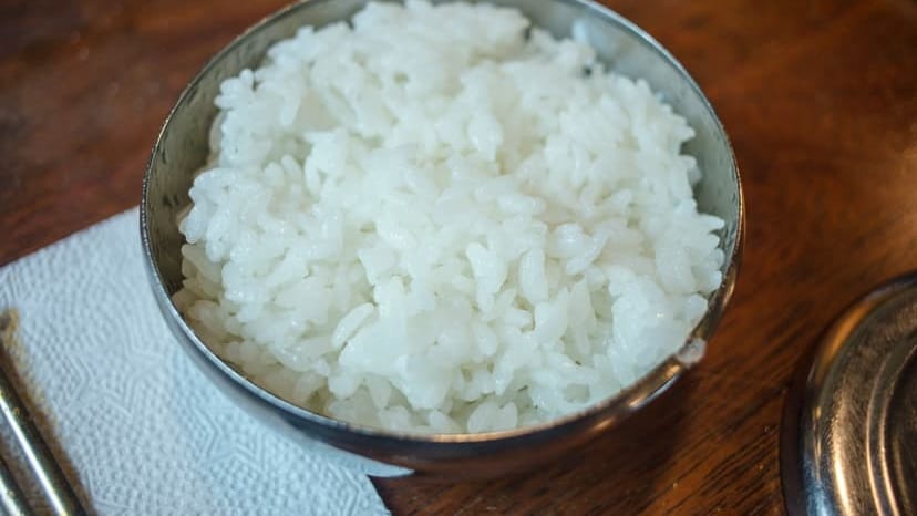 Close-up of steamed white rice in a stainless steel bowl on a wooden table.