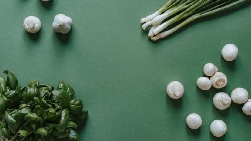 Top-down view of fresh ingredients including basil, mushrooms, garlic, and green onions on a green background.