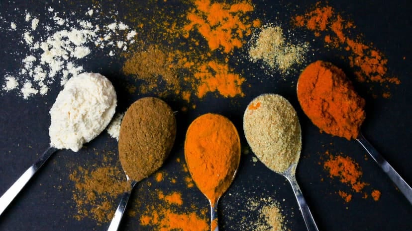 Five spoons of vibrant spices against a black background, showcasing culinary diversity.