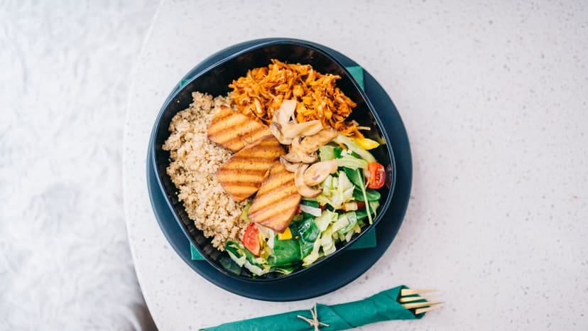A nutritious bowl featuring grilled tofu, quinoa, fresh salad, and mushrooms on a light background.