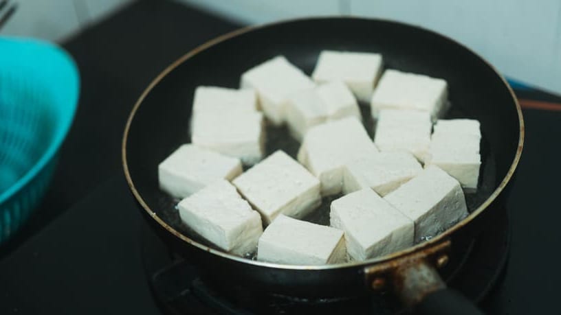 Close-up of white tofu cubes frying in a black non-stick pan.