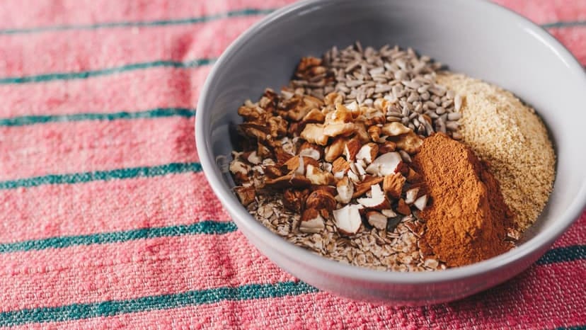 A mix of seeds, nuts, and spices in a bowl on a pink textured cloth, showcasing healthy food.