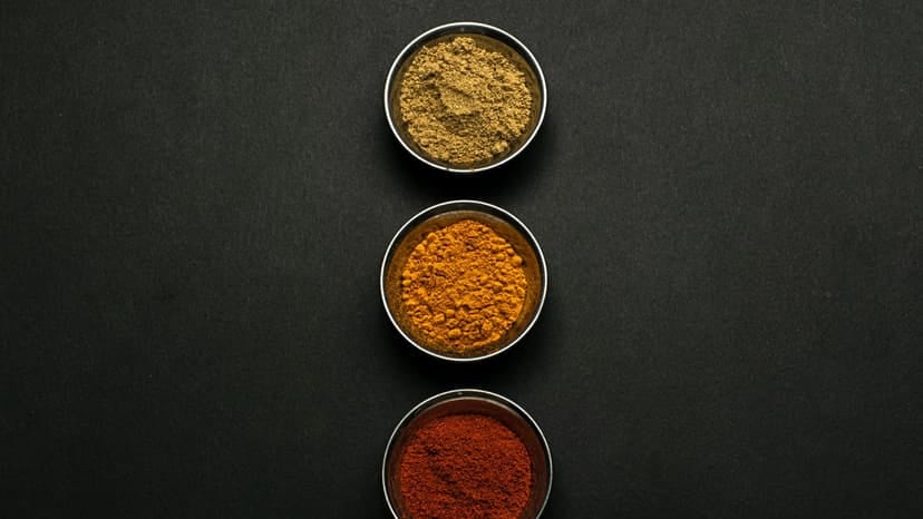 Top view of assorted spice powders in metal bowls showcasing vibrant colors against a dark background.
