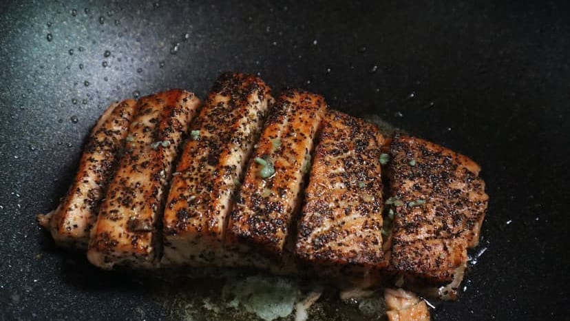 Sizzling grilled salmon steaks with herbs in a non-stick frying pan for a savory meal.