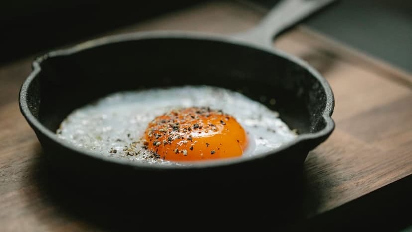 High angle of pan with fried egg with seasoning placed on wooden board in kitchen