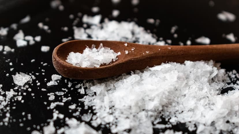 Closeup of wooden spoon arranged with sea salt scattered on table in kitchen