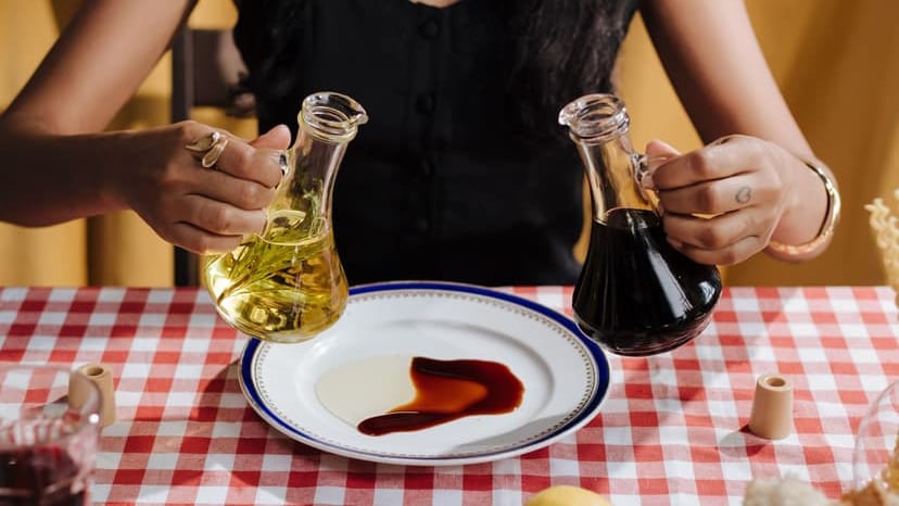 A woman pours olive oil and vinegar on a plate over a red checkered tablecloth.