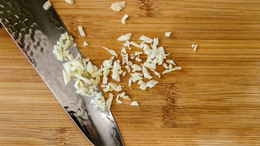 Close-up of chopped garlic on a wooden cutting board with a stainless steel knife.