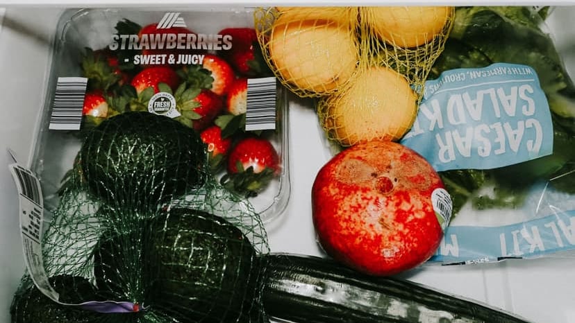 A variety of fresh fruits and vegetables including avocados, lemons, strawberries, and lettuce in a fridge drawer.