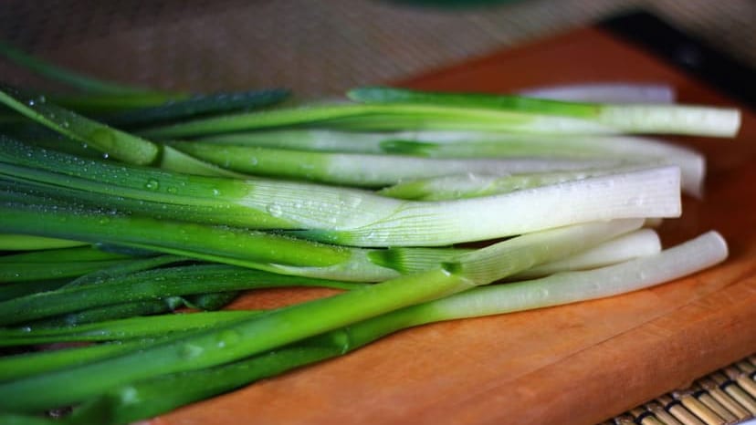 Close-up of fresh green onions on a wooden cutting board, showcasing their vibrant color and texture.