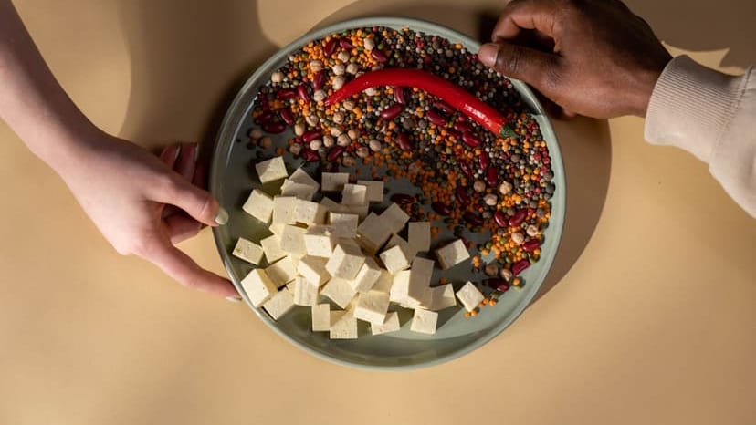 A diverse plate with tofu, legumes, and a chili pepper. Hands shown.